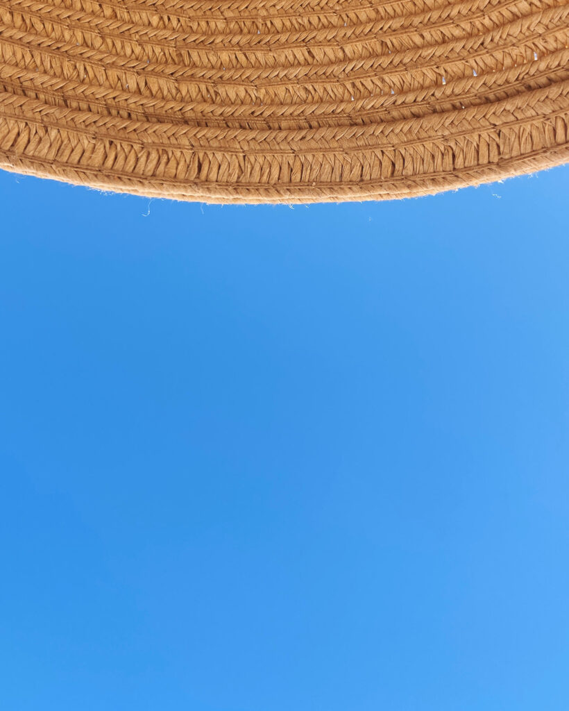 Photograph of blue sky with the brim of a straw hat at the top of the frame.