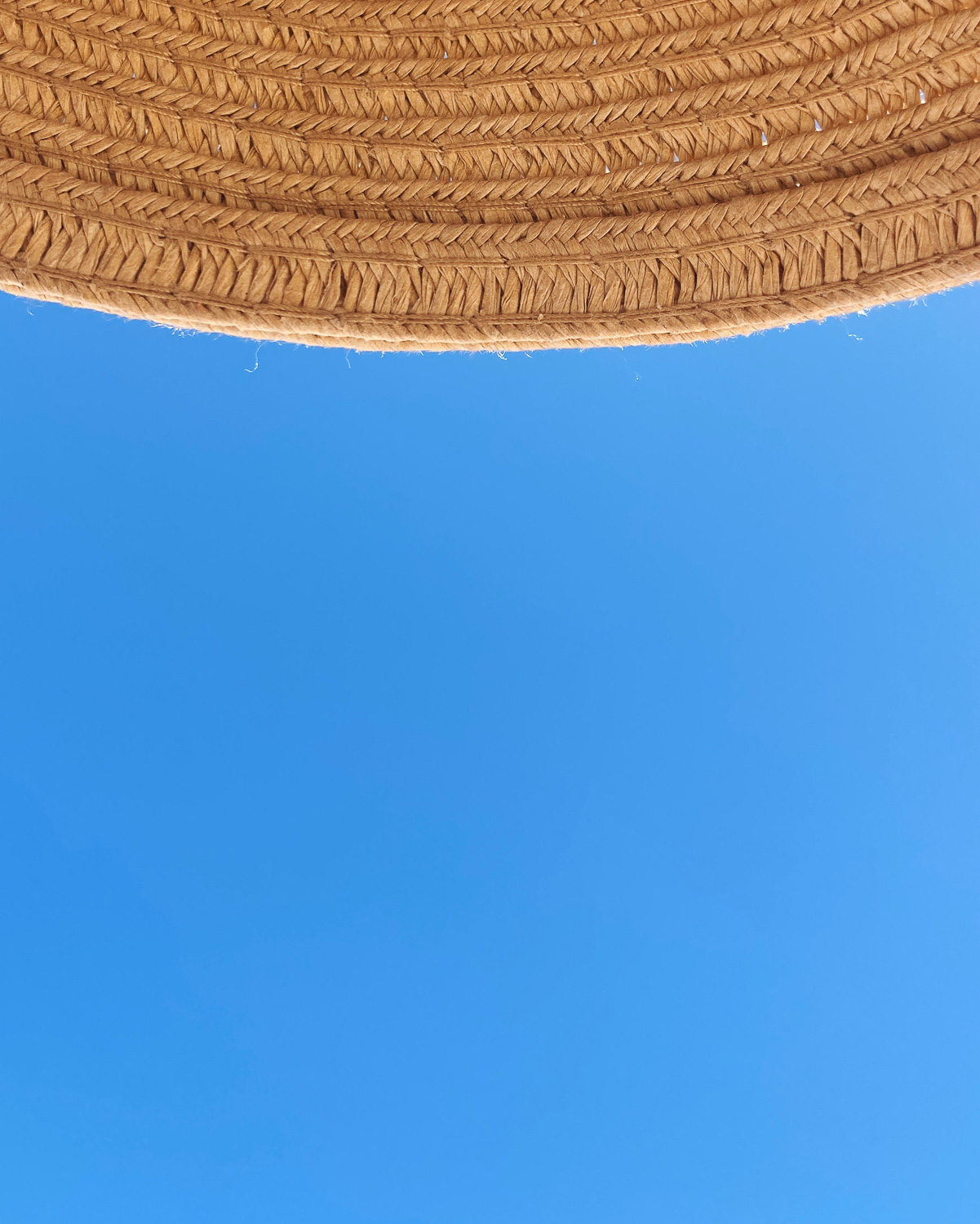 Taking in the warmth. Photograph of blue sky with the brim of a straw hat at the top of the frame.