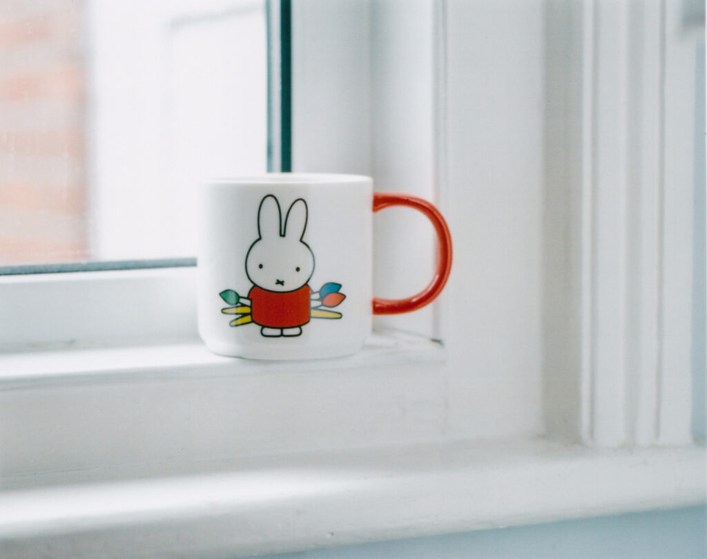 Photograph of a mug with a picture of Miffy and an orange handle, on a window frame