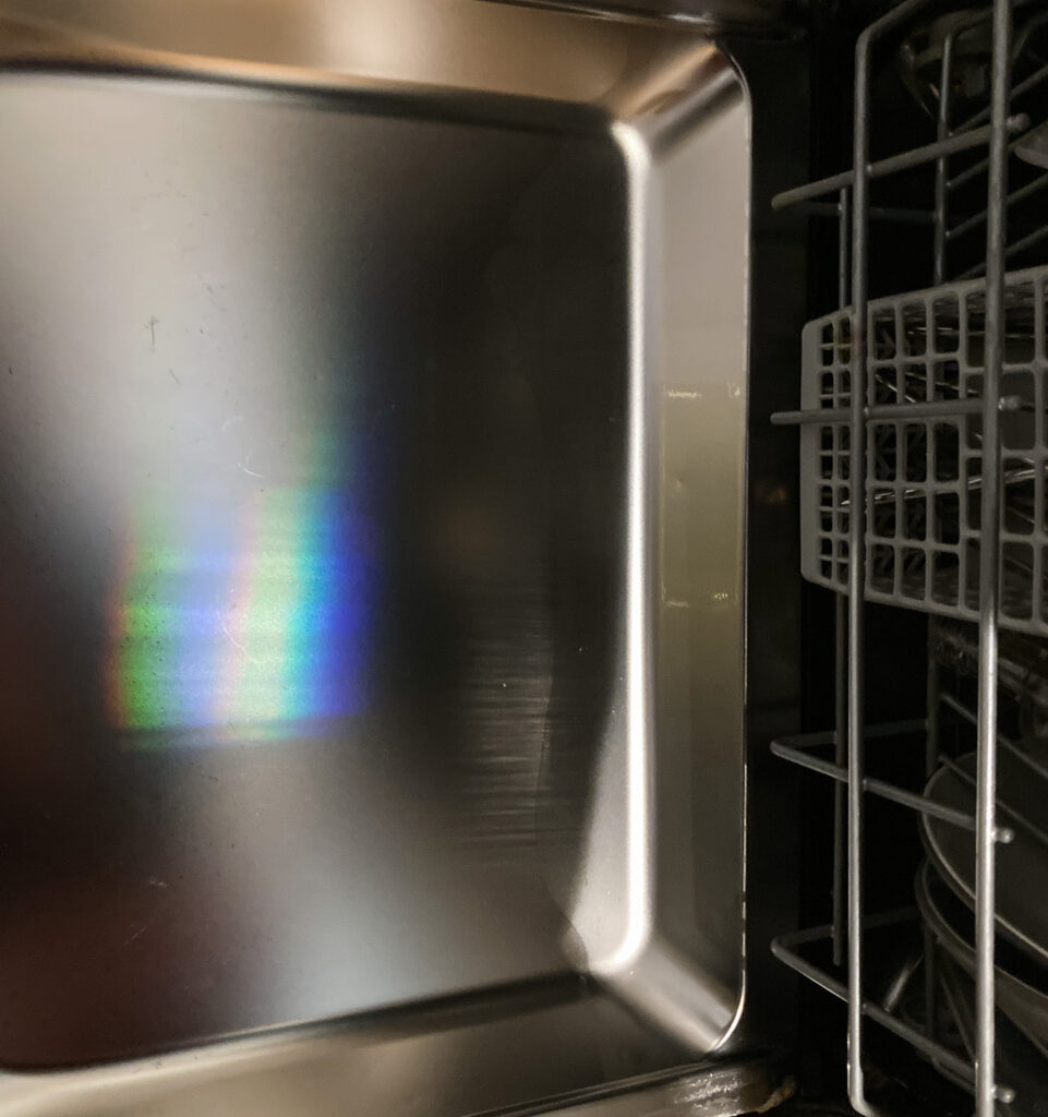 Photograph looking down from the side of a small dishwasher, with the door open showing a streak of rainbow, and the drawers visible to the right.