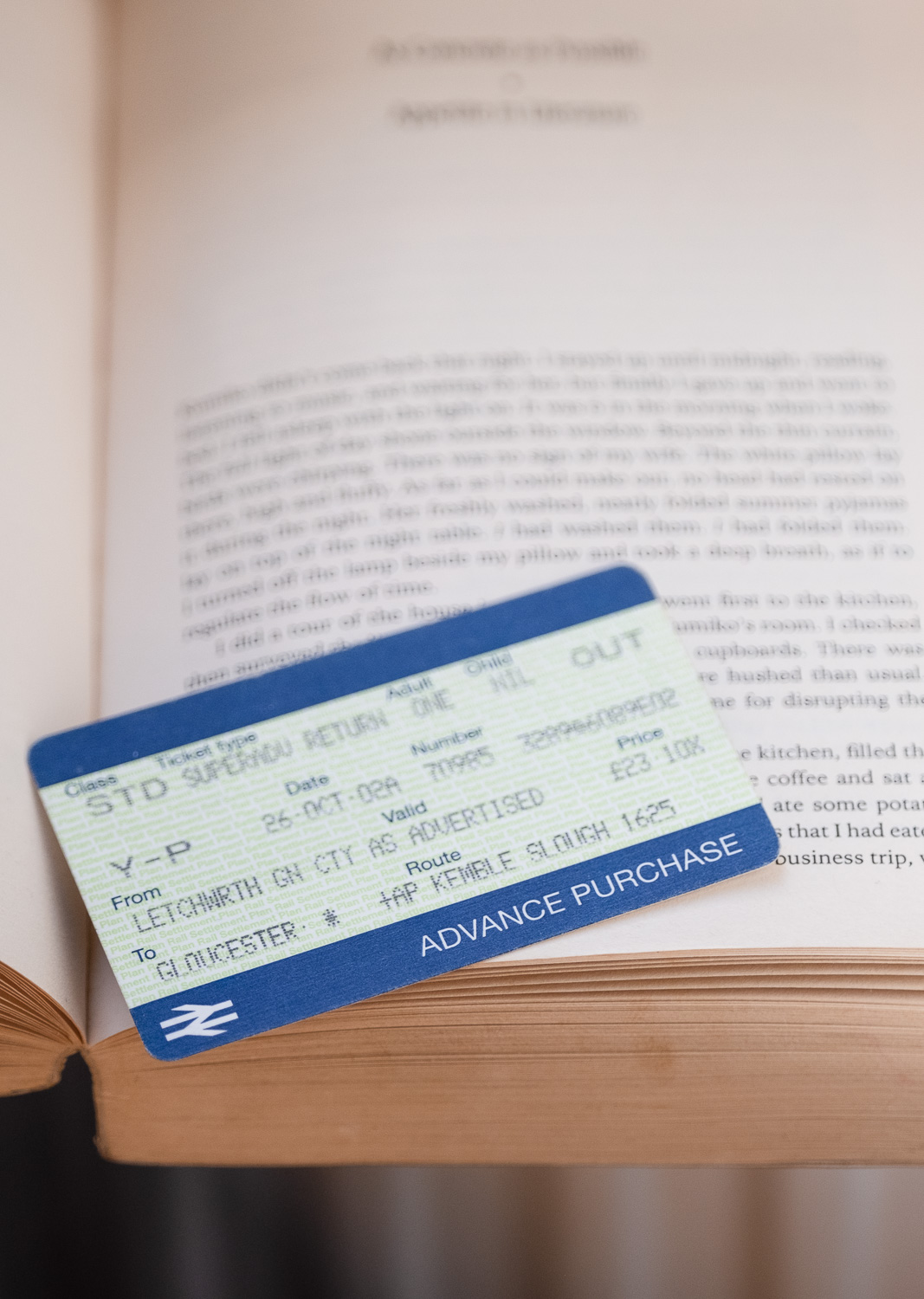 Someone else's bookmark. Was this where they stopped reading? Were they visiting someone? Did they have a nice time? Photograph of a train ticket balanced on the pages of an open book, blurred words on the page visible behind. It's a young person's superadvance return from Letchworth to Gloucester dated 26 October 02, £23.10