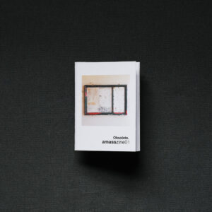 Photograph of a small foldy zine on a dark grey background. The cover shows an empty noticeboard with signs of wear, and text saying 'Obsolete. amasszine01'