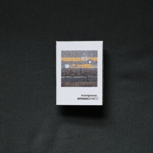 Photograph of a small foldy zine on a dark grey background. The cover shows a photograph of a smashed blue mug on double yellow lines against a curb, and text saying 'Incongruous. amasszine02'