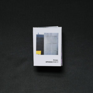 Photograph of a small foldy zine on a dark grey background. The cover shows a grey wall with greasy handprints smeared on it, with a darker wall and a yellow square slightly behind and to the left and text saying 'Smear. amasszine02'