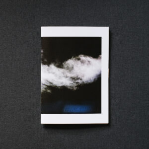 Photograph of TRIVIAL MATTER 01, a photo zine, on a dark grey fabric background. Shown is the front cover with a photograph of steam on a dark background.