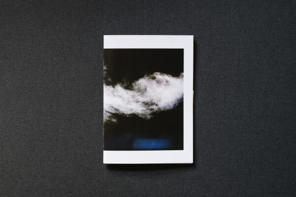 Photograph of TRIVIAL MATTER 01, a photo zine, on a dark grey fabric background. Shown is the front cover with a photograph of steam on a dark background.