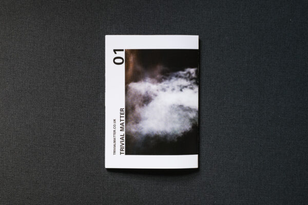 Photograph of TRIVIAL MATTER 01, a photo zine, on a dark grey fabric background.