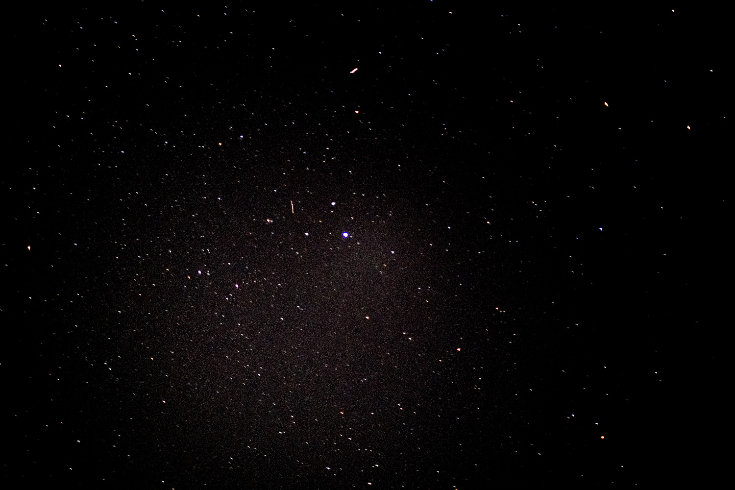 Some time staring at the sky, looking for meteors without a tripod. Photograph of the night sky with stars visible on a clear night. A tiny light trail towards the centre could possibly be a meteor?