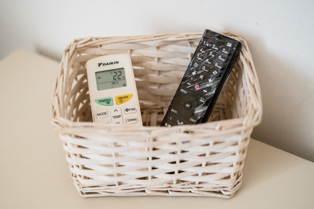 Photograph of a basket with an air conditioning and TV remote control, wrapped in celophane.