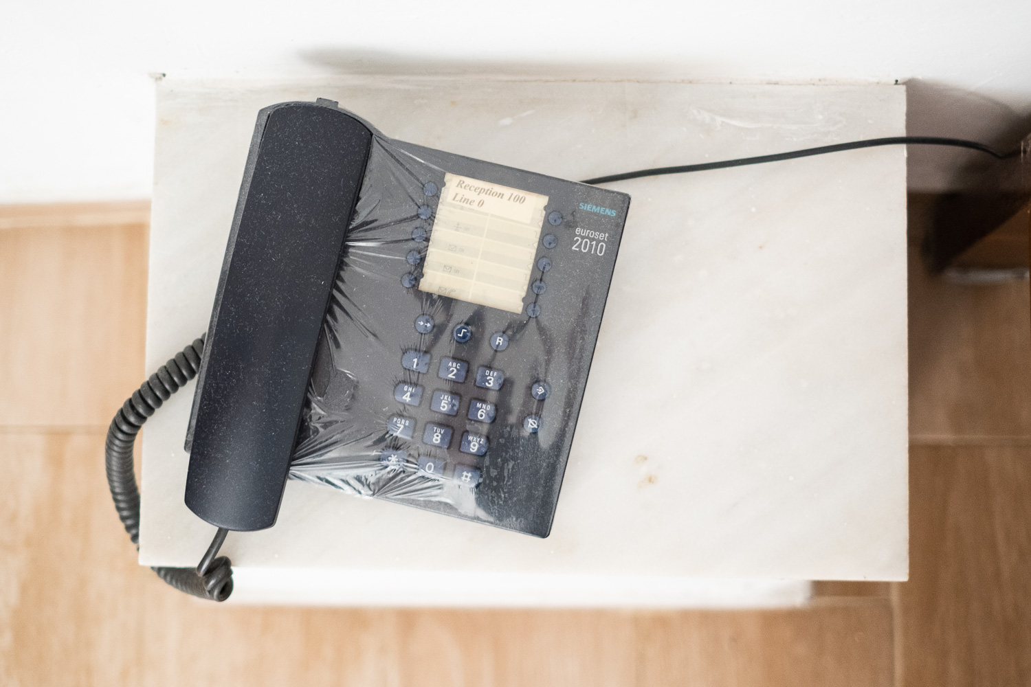 Good intentions. Photograph of a telephone with plastic wrap over the main body and keypad, but a layer of dust over the top.