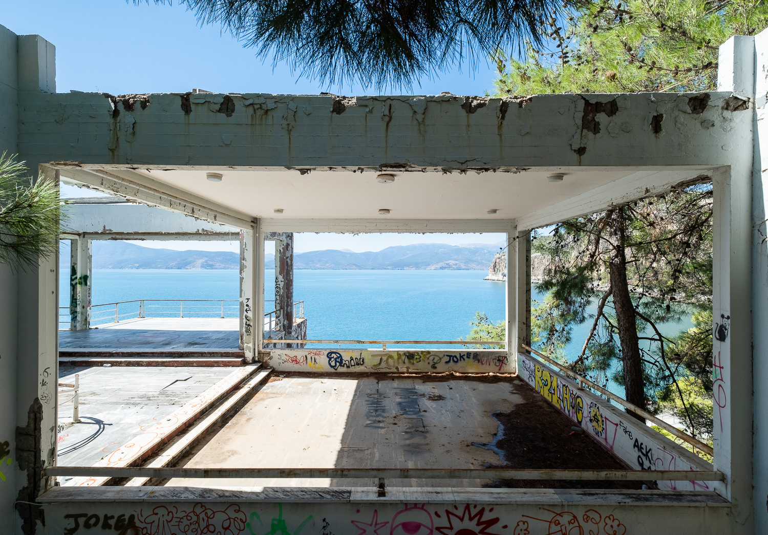 Room with a view. Photograph of an abandoned shell of a hotel, with a view of the sea and mountains behind.