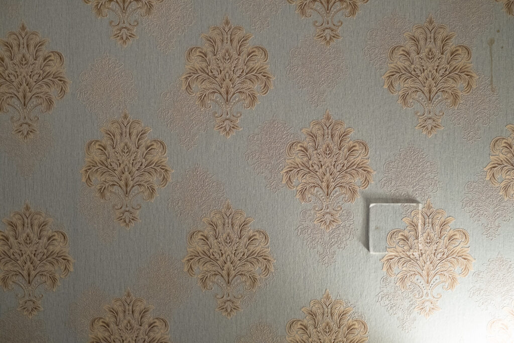 Photograph of a wall with ornate wallpaper with a square protruding, matched up with the wallpaper behind.