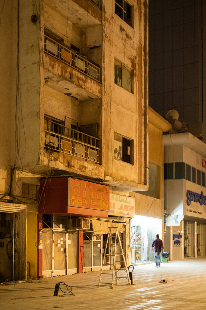 A photograph of a street scene in Doha, Qatar, showing an older, rundown building with a ladder in the foreground. Doha tore down and rebuilt most buildings in preparation for the World Cup 2022.