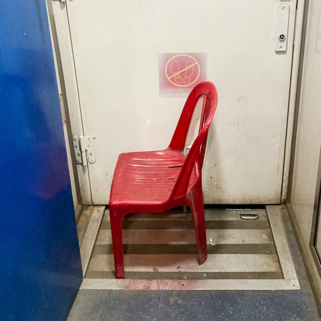 A small red plastic chair by a door, on a train.