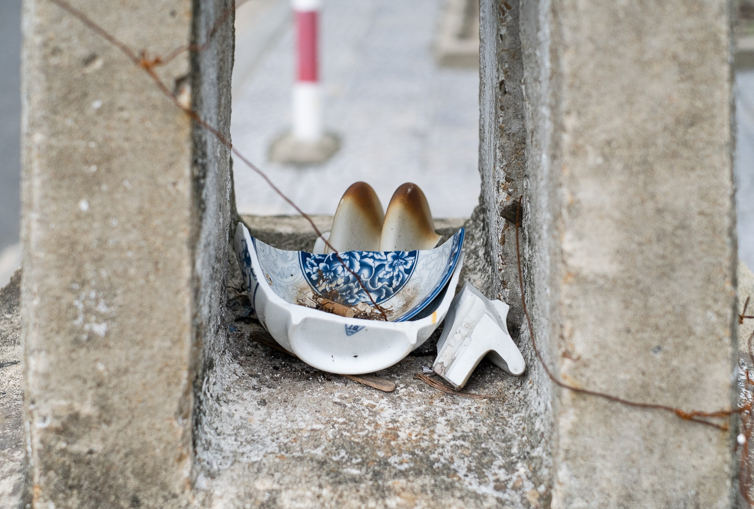 Photograph of a broken ceramic bowl with ornate blue and white pattern, with part of a ceramic toast wrack with scorch marks on it, all within a concrete block.