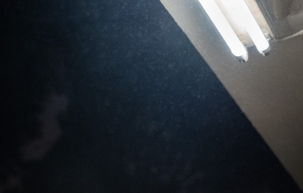 Photograph showing fluorescent strip lights in the top right with raindrops all around and a dark sky to the right.