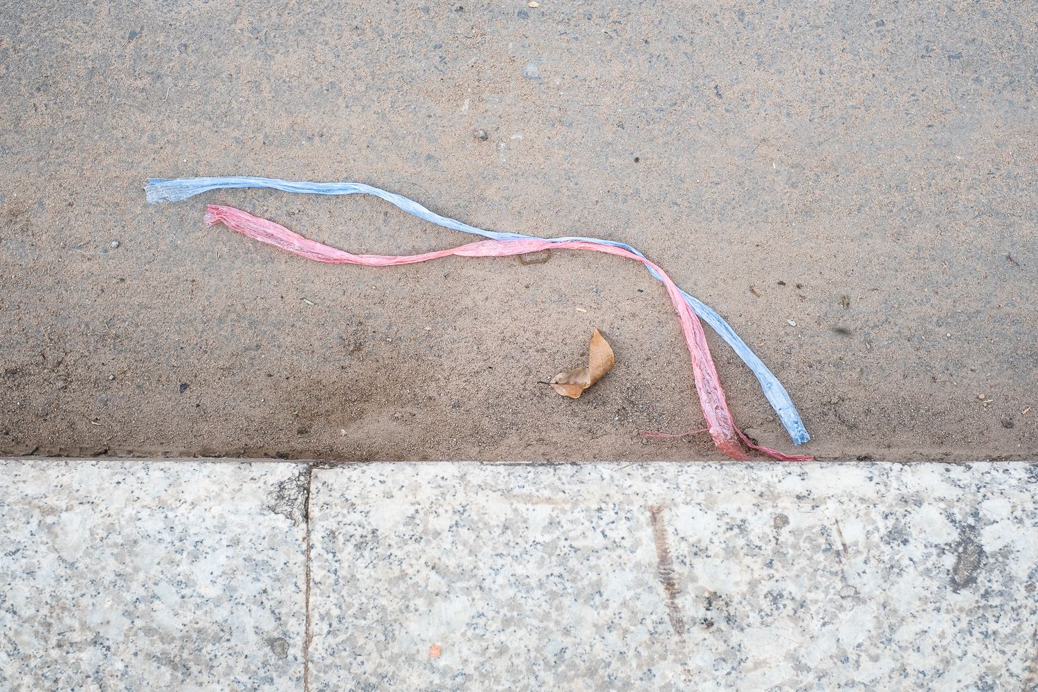 Photograph of blue and pink plastic string in a gutter at the side of the road.