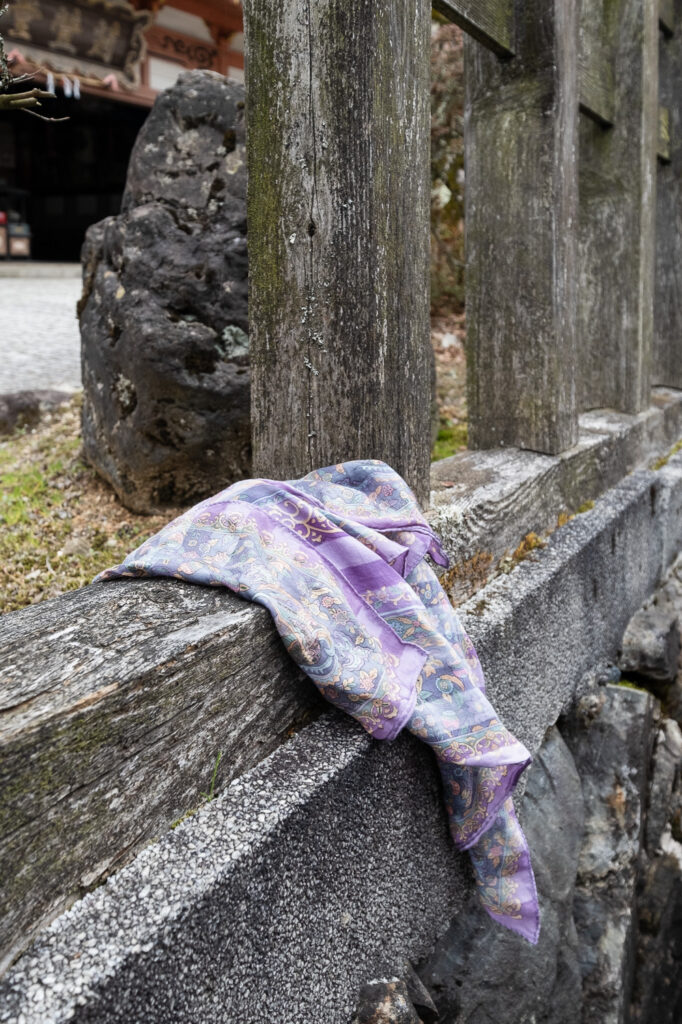 Photograph of a purple patterened scarf tied to a wooden fence.