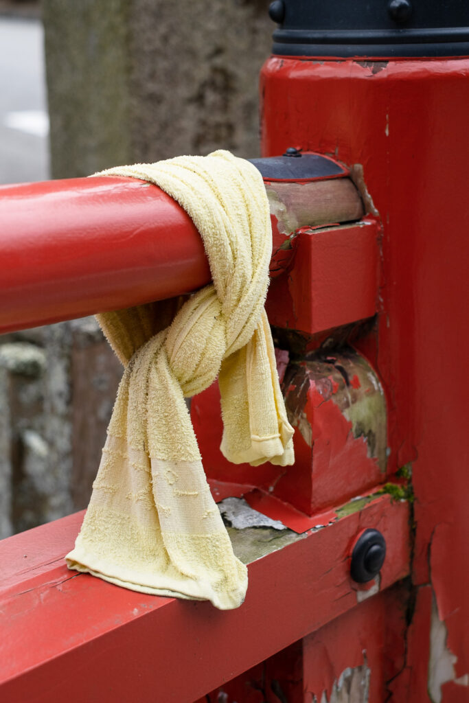 Photograph of a yellow towel tied to a wooden fence that's painted red.