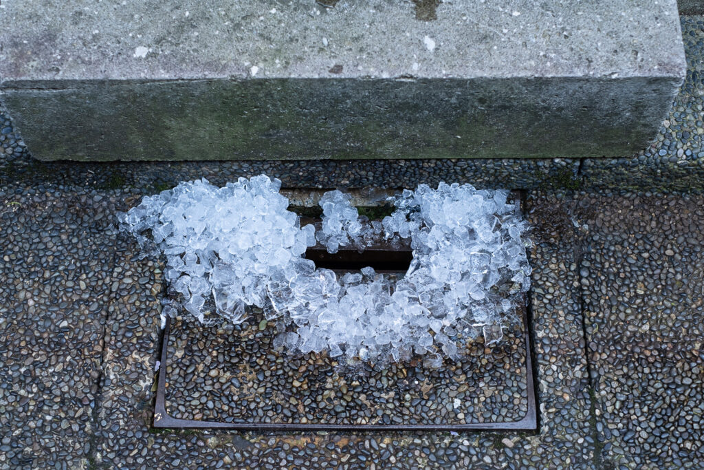 Photograph of a pile of ice around the edges of a drain, in front of a concrete step.