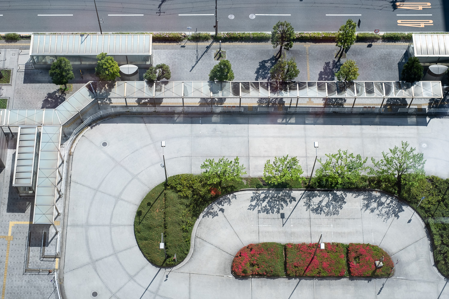 Photograph looking down on a turning area for cars, with flower beds and trees and covered bus stops around the edges.