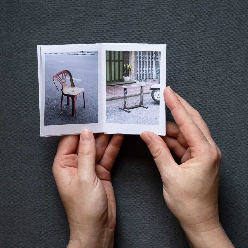 Photograph of 'Do not park your cars here', a zine by Jayne Lloyd, showing the A7 sized zine being held in front of a dark grey fabric background.