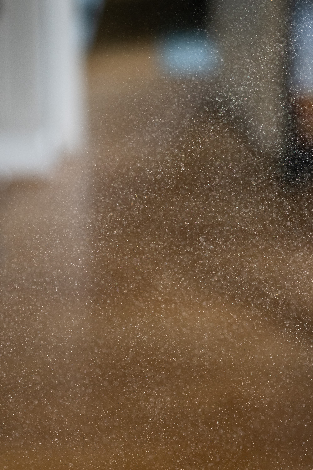 Photograph of a cloud of icing sugar catching the light, with a wooden floor and doorway blurred in the background.