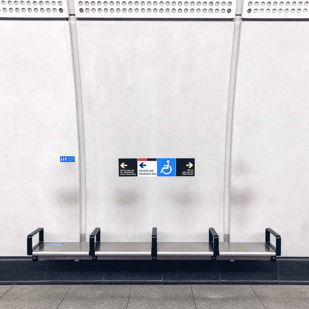 Photograph of a bench on the Elizabeth Line platform, with 4 marks on the wall where people have leaned against it.