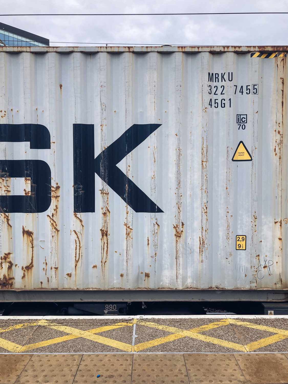 A container on freight train, zooming in to show a yellow triangle with 'SUPER HEAVY' written on it.