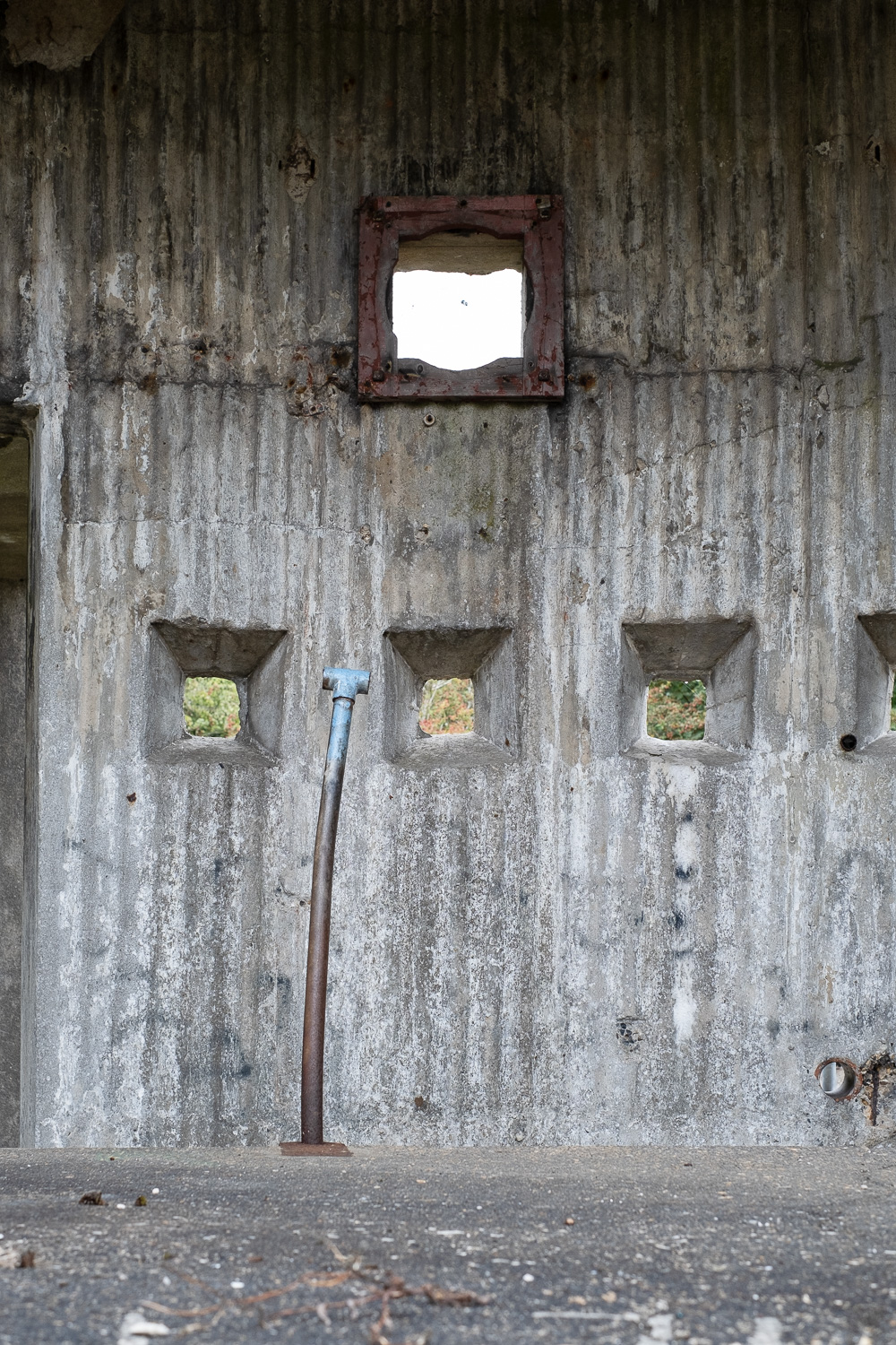 A metal pole with light blue paint at the top, in front of a concrete wall with small square windows and corrugated texture, Harwich, Essex, UK