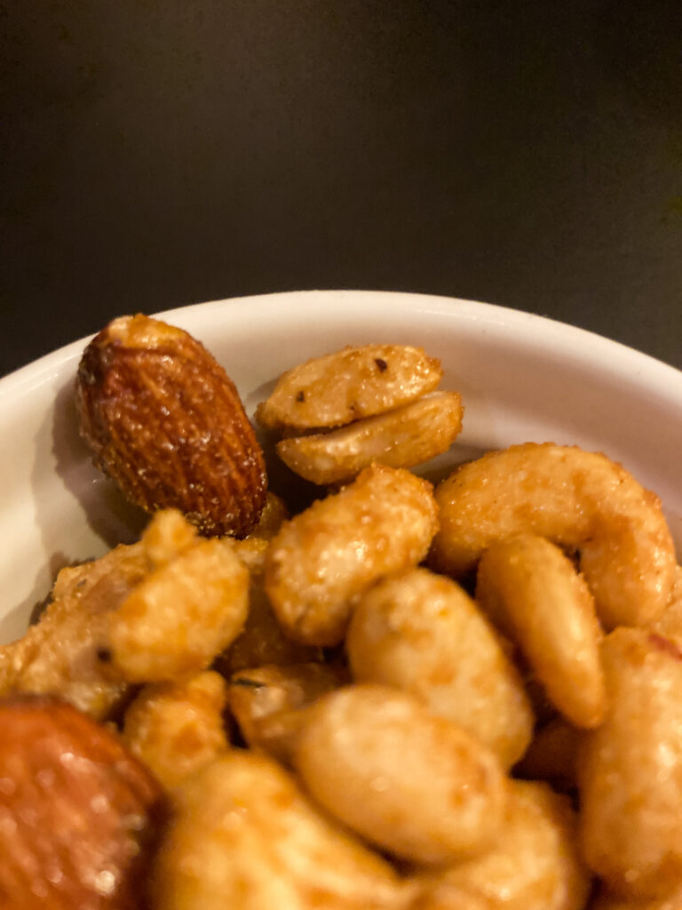 Photograph of a white ceramic bowl filled with nuts with a flavoured coating on them. The peanut in the centre of the frame has 2 dots on the top half and the line across the middle makes it look a little like a small smiling face.