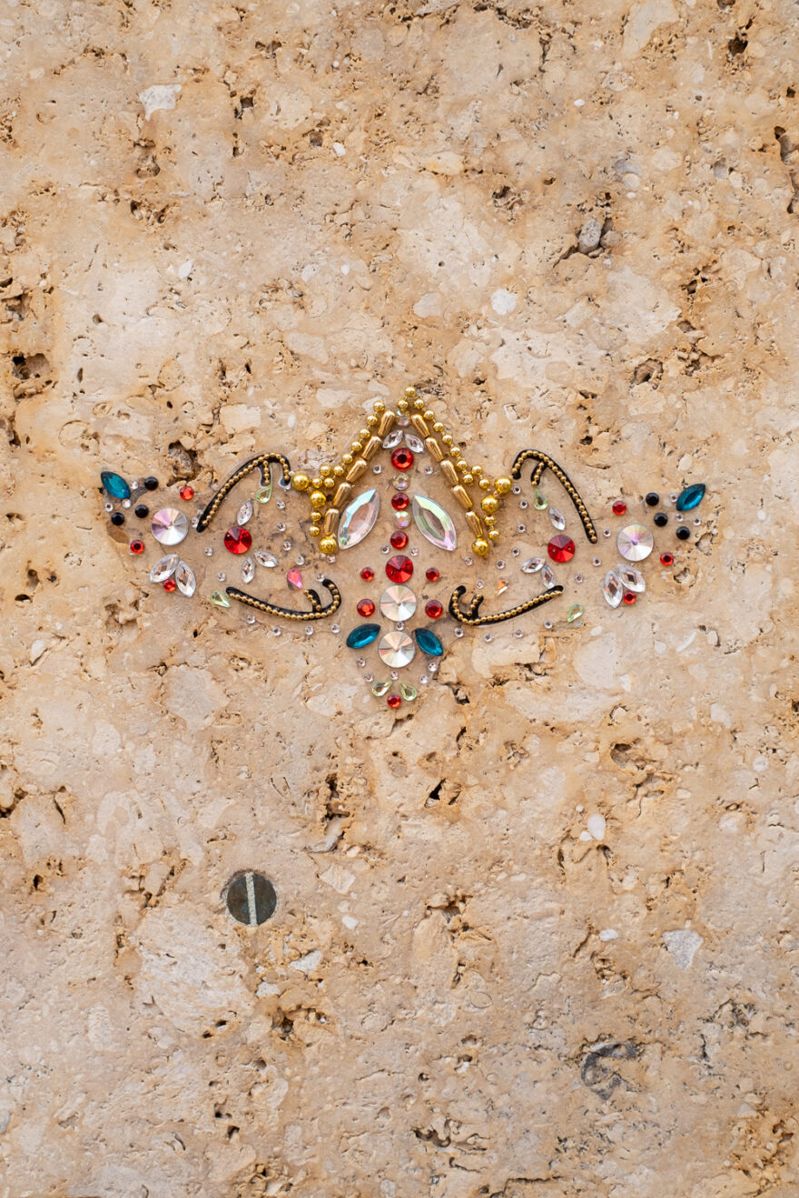 Copenhagen, Denmark, August 2024. Photograph of an arrangement of sequins meant to be worn on a forehead as decoration, stuck on a mottled beige wall.