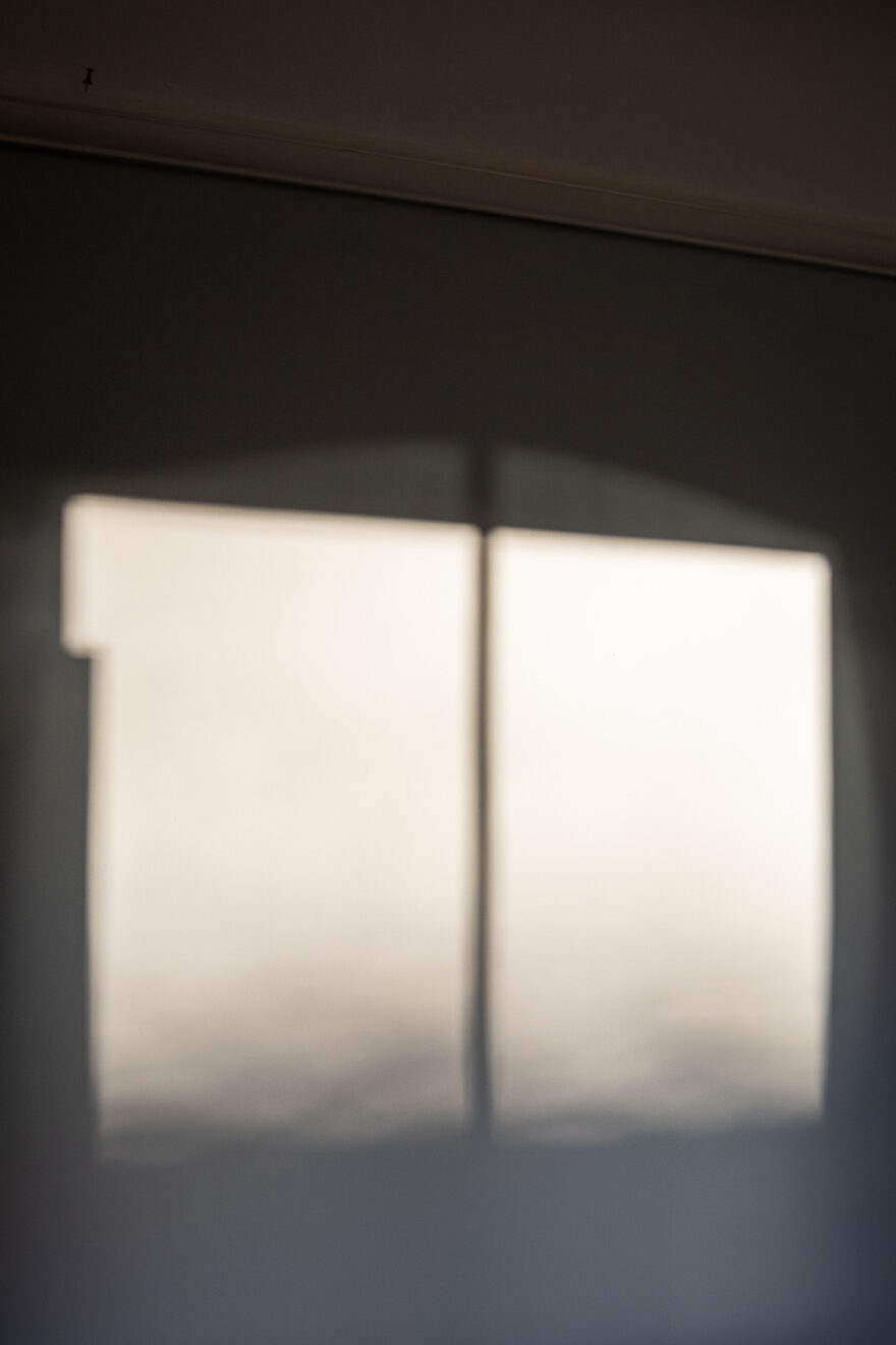 Photograph of a wall with two bright rectangles in the centre, the pattern of low winter sunlight shining through a window and casting the shadow of the frame on the wall. At the top of the frame a picture frame with a red push pin to the left is visible.