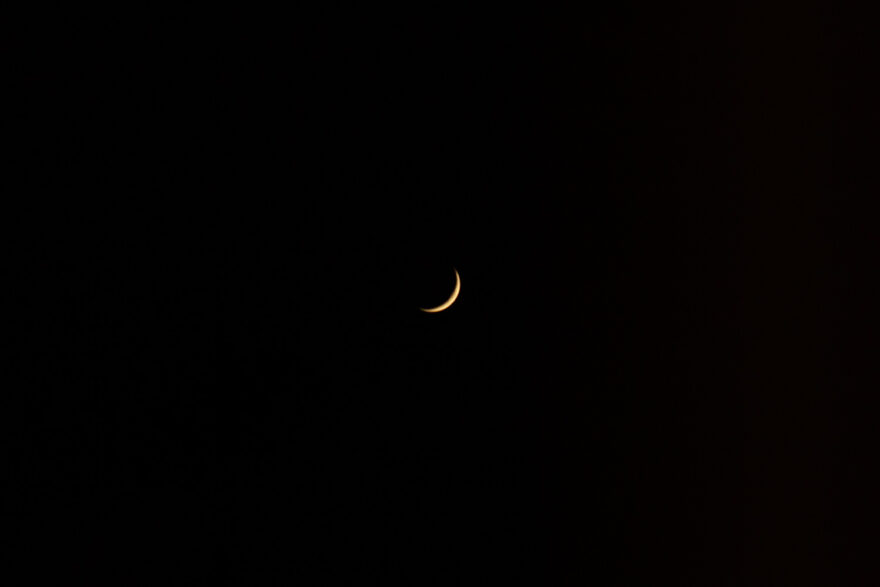 Photograph of a the moon in a black sky, with only a tiny golden part visible.