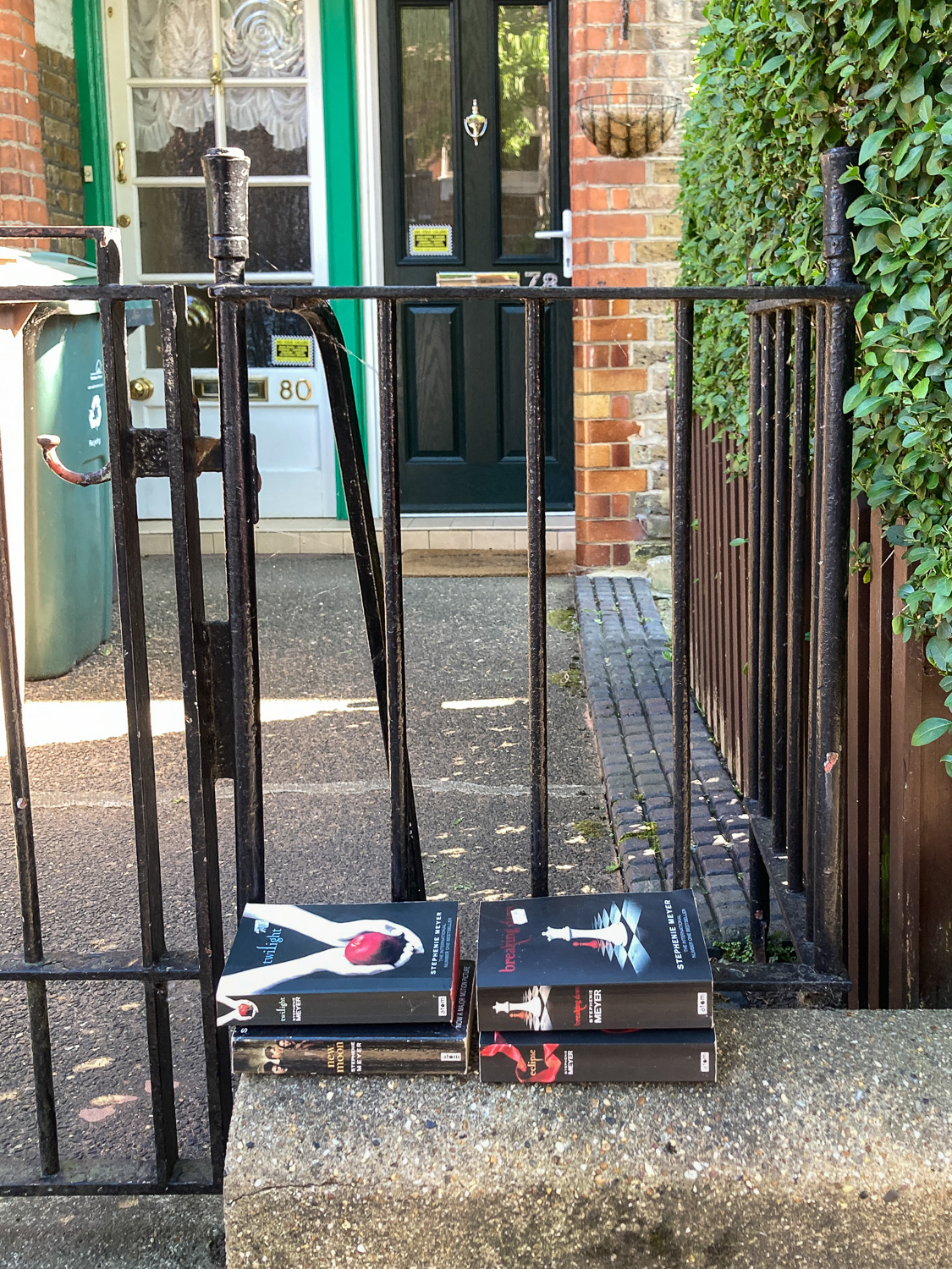 Photograph of 4 paperback books, the full Twilight Saga, stacked on a wall in front of a house.