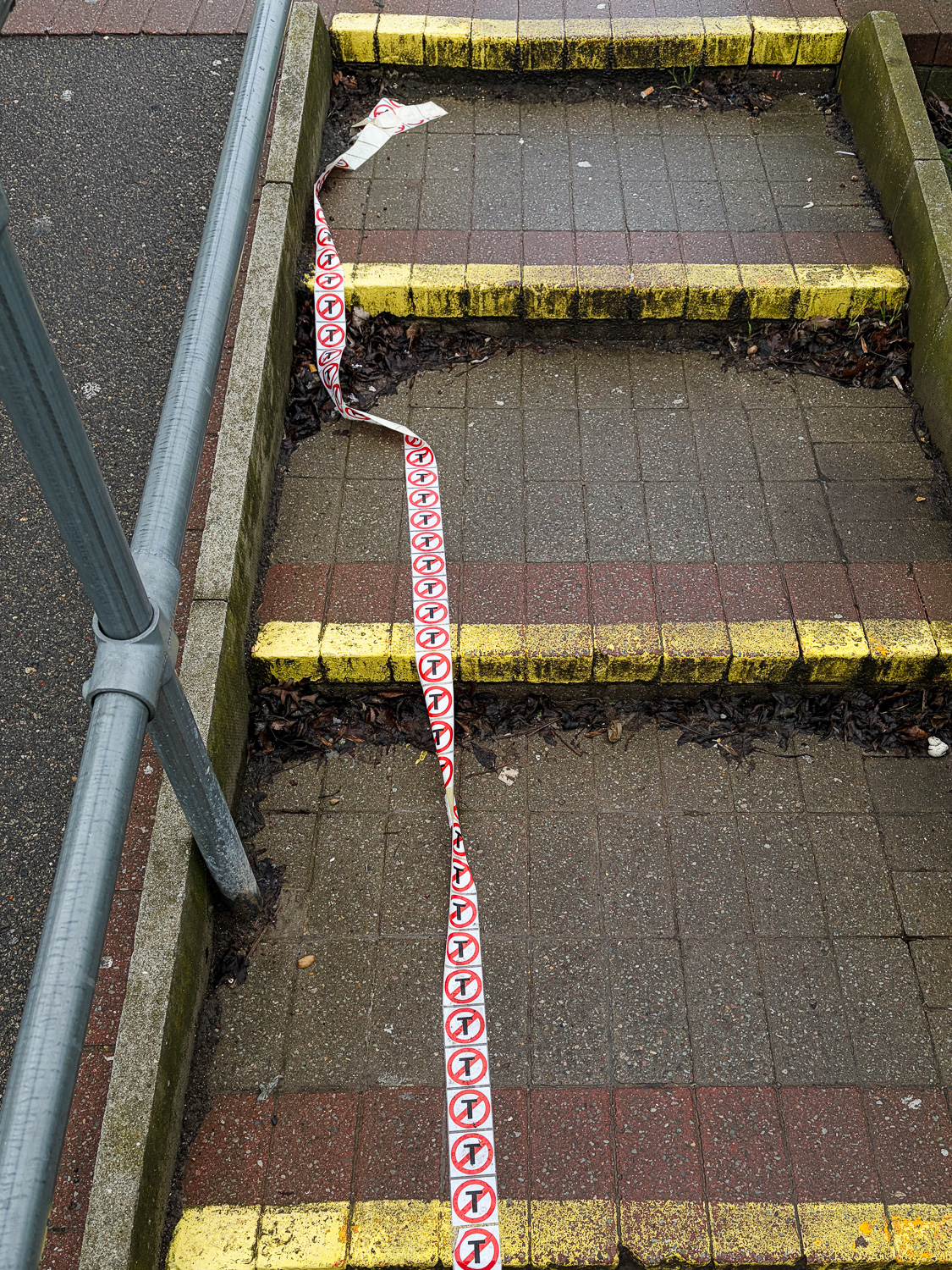 Photograph of a long length of stickers with a letter T with a red circle and crossed through it, stretching across long steps with yellow paint marking the edges.