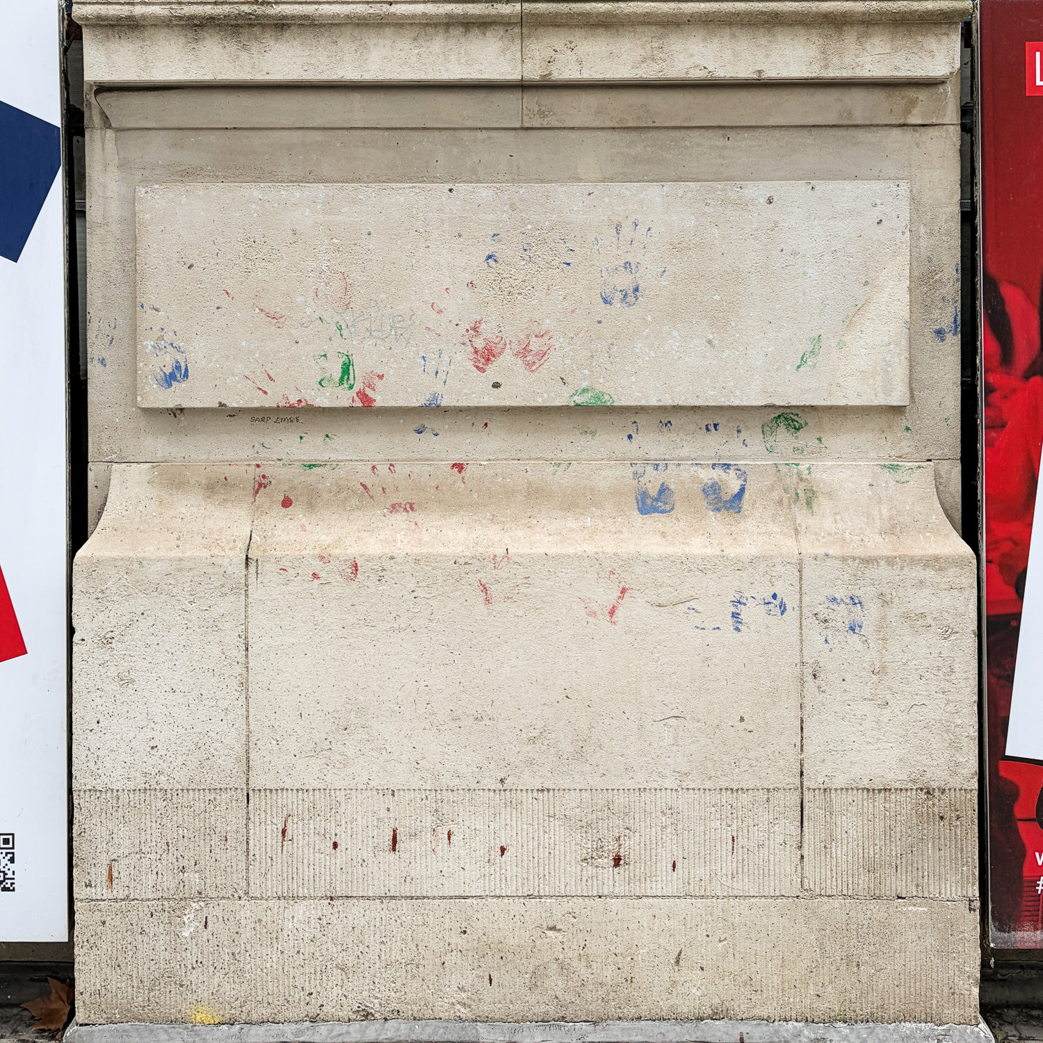 Photograph of a cream coloured pillar-like wall feature covered in red, blue and green handprints.