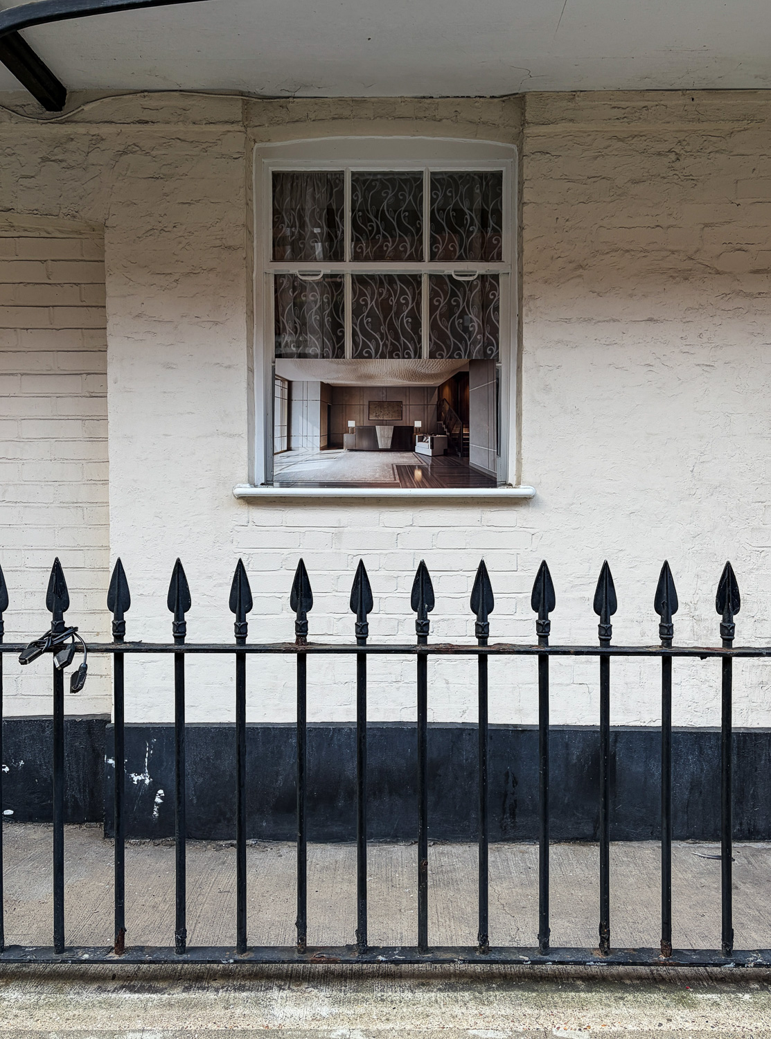 Photograph of a photographic print of a luxurious interior propped up on a wood framed window, in a cream-painted brick wall, with a wrought iron black fence in the foreground.