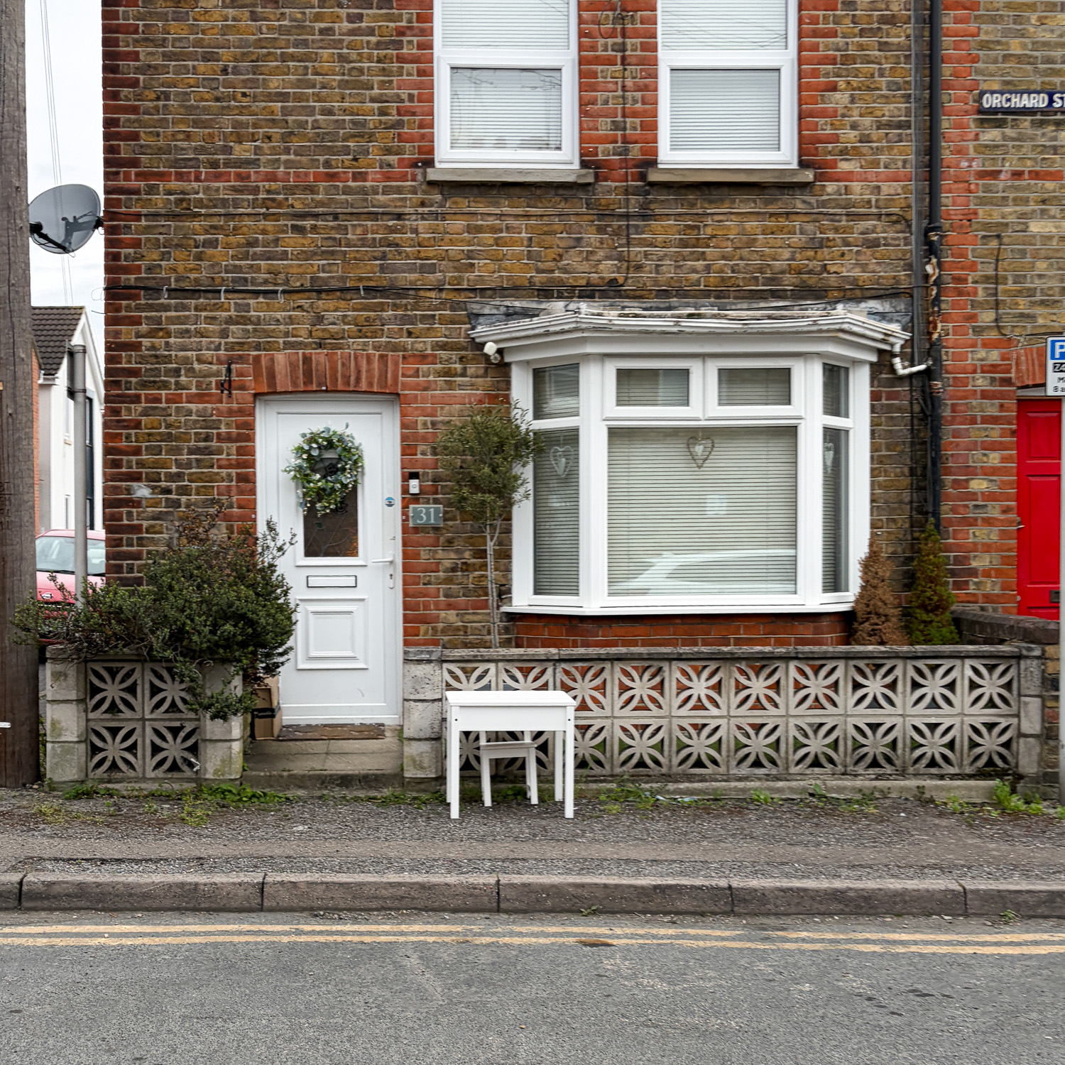 Photograph of a child's white desk and chair on a pavement in front of a house with white door and bay window.