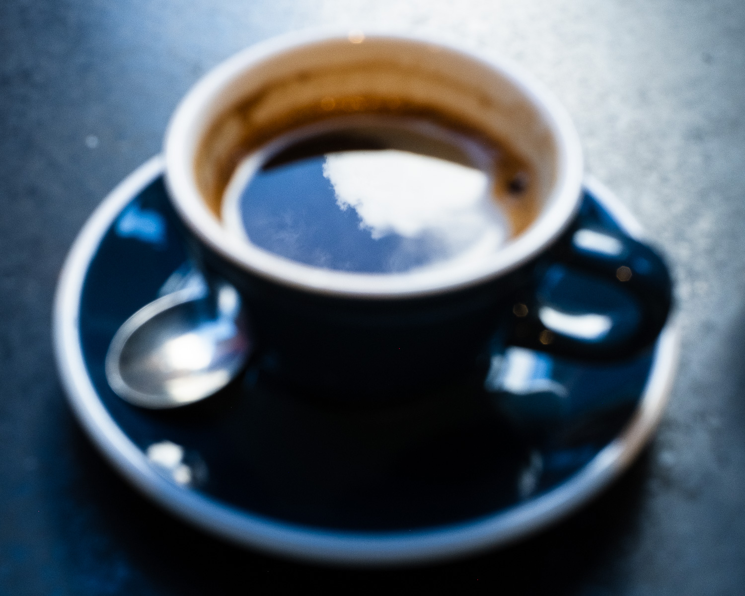 Photograph of a cloud reflected on the surface of a black coffee in a cup and saucer.